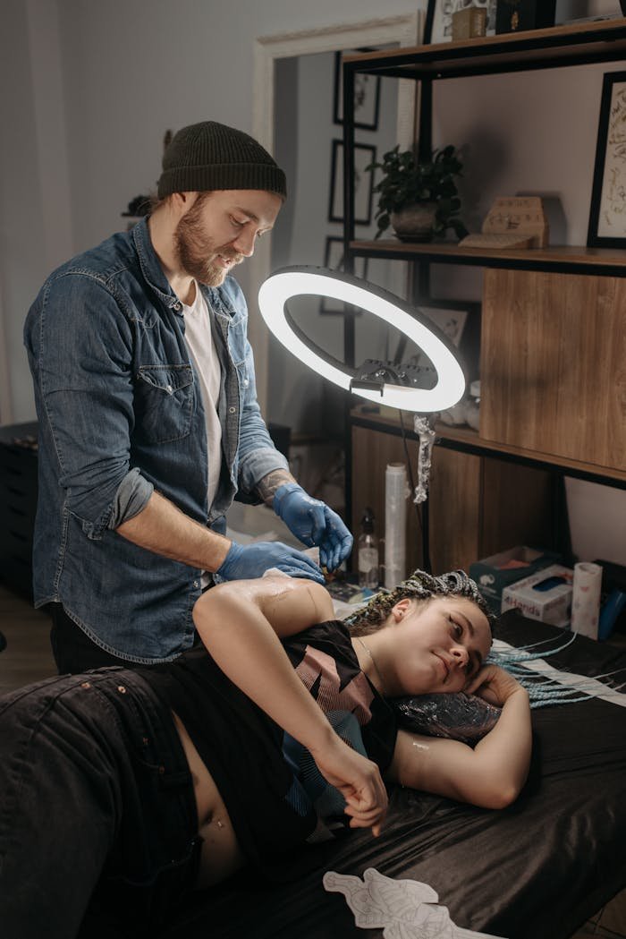 social-feed-img-04 A tattoo artist creating a new design on a womans arm in a modern studio setting.