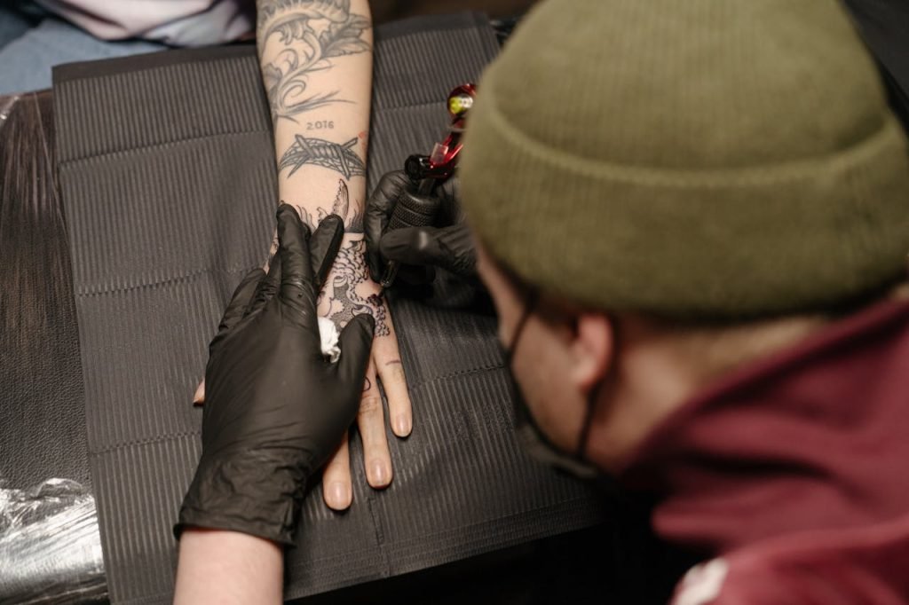 Tattoo artist using machine to ink elaborate design on clients hand in studio.
