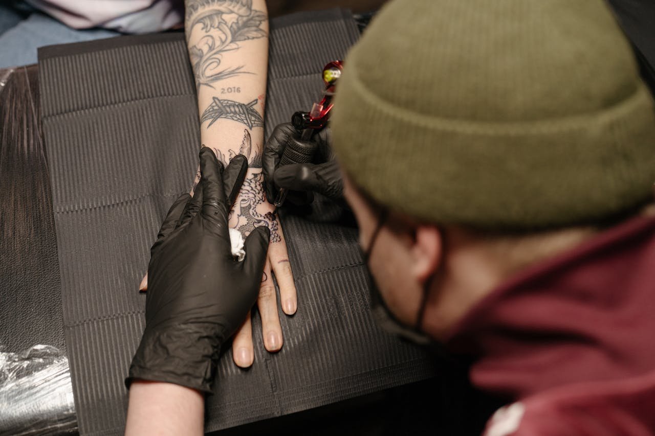 social-feed-img-03 Tattoo artist using machine to ink elaborate design on clients hand in studio.